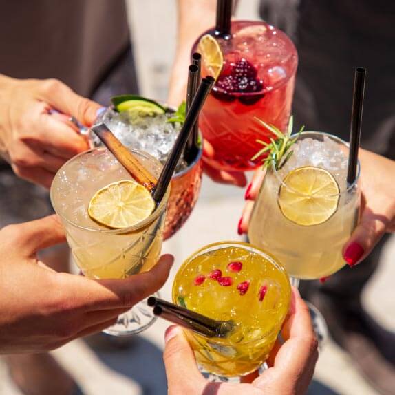 Five glasses of brightly coloured drinks containing ice, straws and fruit